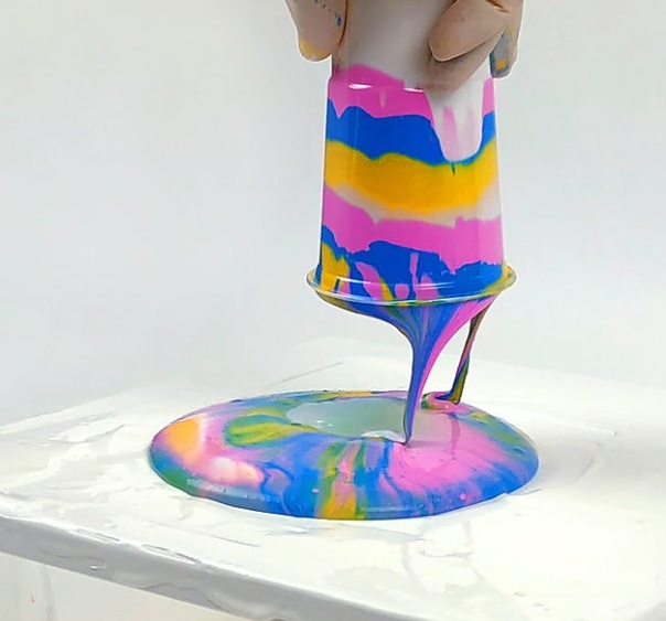 Acrylic Paint Pouring - cup with mulitiple colors of paint turned upside down dripping paint onto canvas underneath