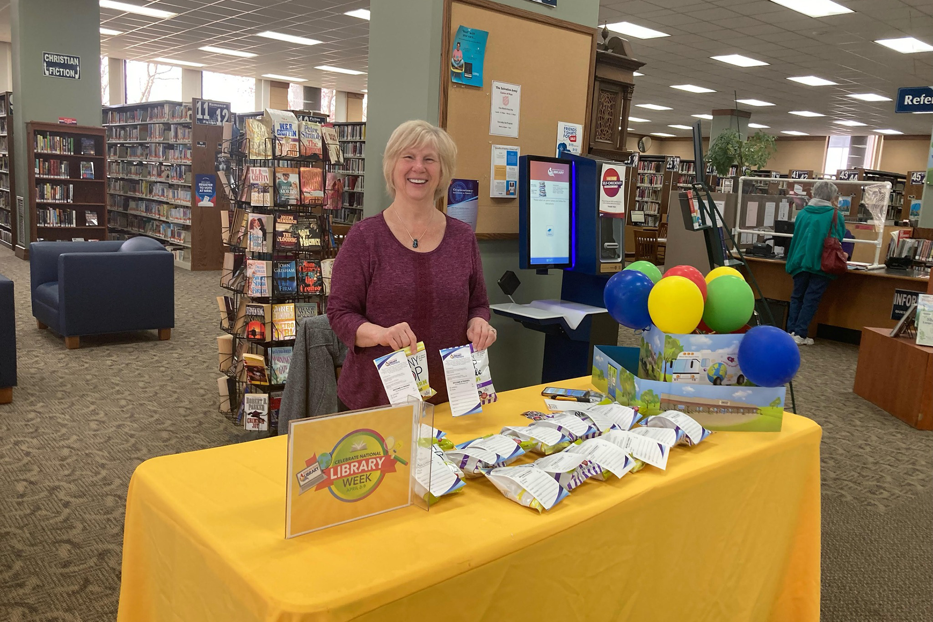 Smiling woman at a table with Library Week merch
