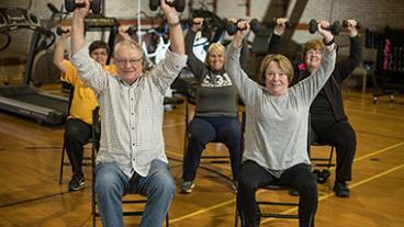 seniors sitting in chairs and lifting weights above their heads