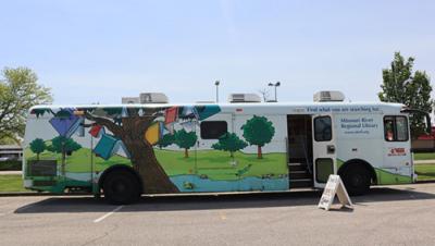 Large bookmobile bus in a parking lot. Painted trees on the side of the bus.
