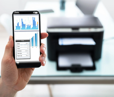 Phone held up showing a print preview. There is a printing spitting out a piece of paper in the background.