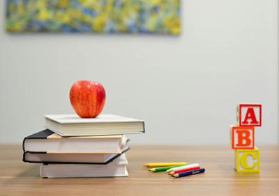 Stack of four books with an apple of top, colored pencils, and three ABC blocks stacked.